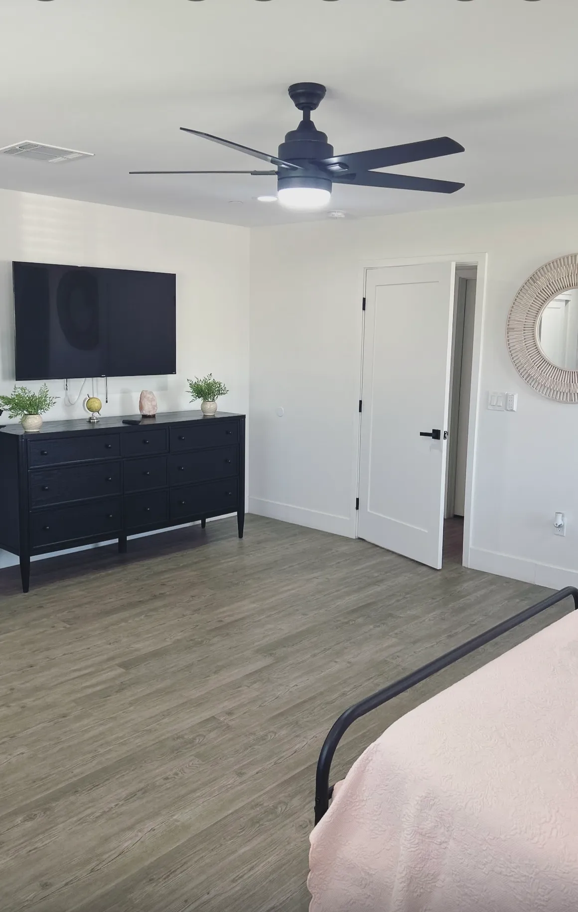 Resident bedroom with black dresser, wall-mounted TV, and ceiling fan