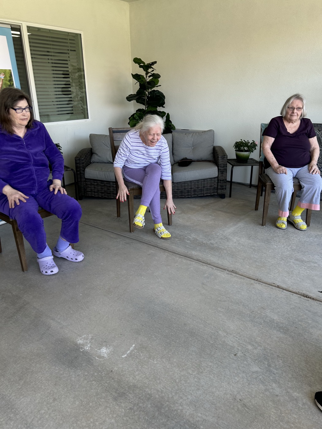 A resident laughs during a seated stretching exercise at a Living Gracefully physical therapy class on the patio